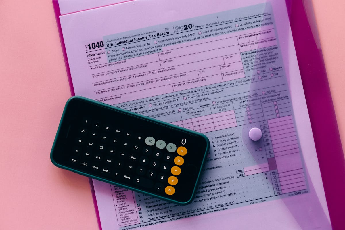 Photo by Nataliya Vaitkevich Tax form 1040 with a calculator on a pink background, highlighting finance and accounting themes.